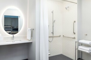 A modern bathroom with a round mirror, a shower with grab bars, and a towel rack.