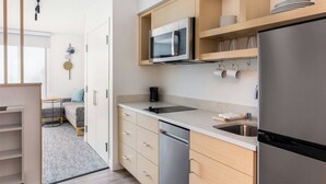 A modern kitchen with a stainless steel refrigerator, a microwave, and a dishwasher. There is a sink with a countertop, and wooden cabinets above.