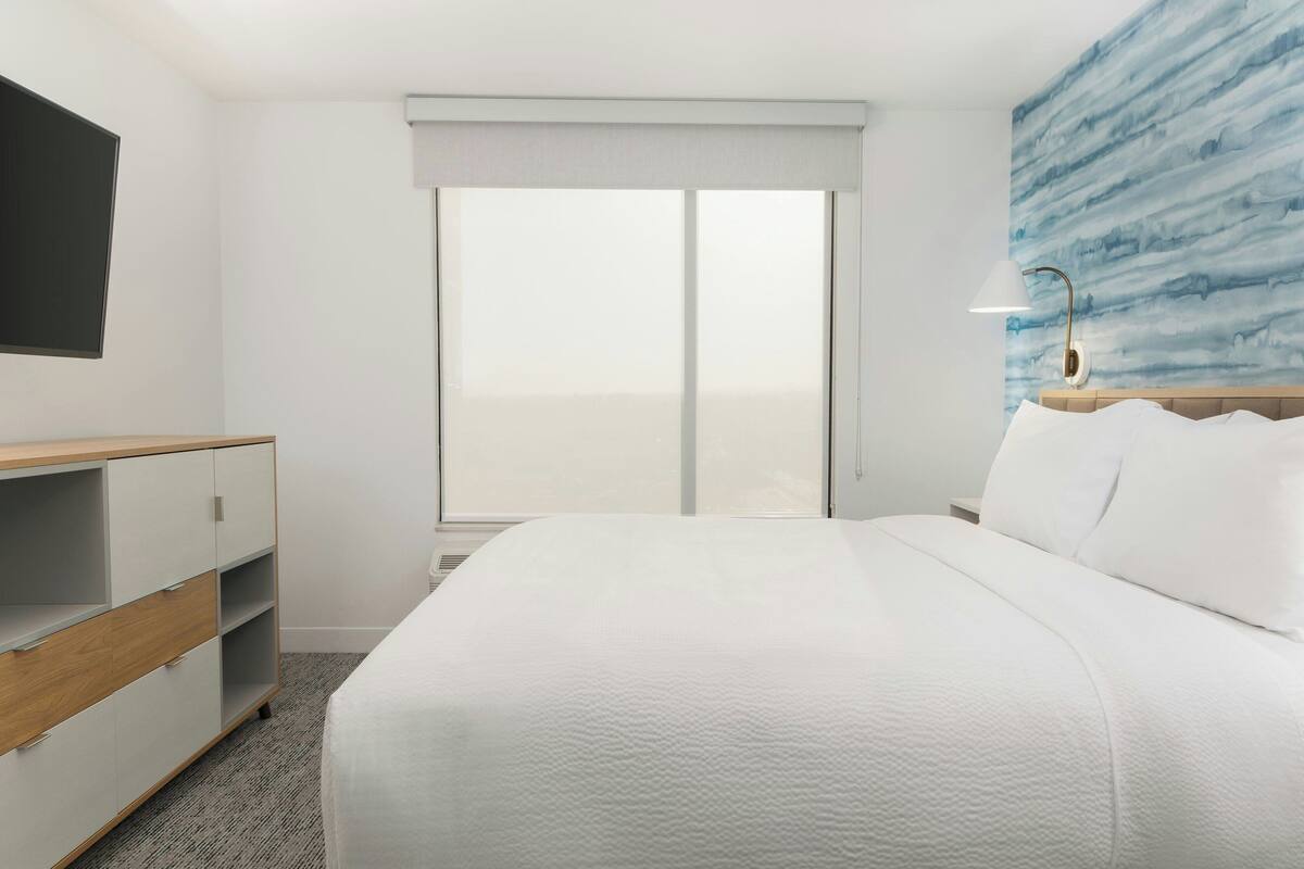 Et hotelværelse med seng, skrivebord og stort vindue.