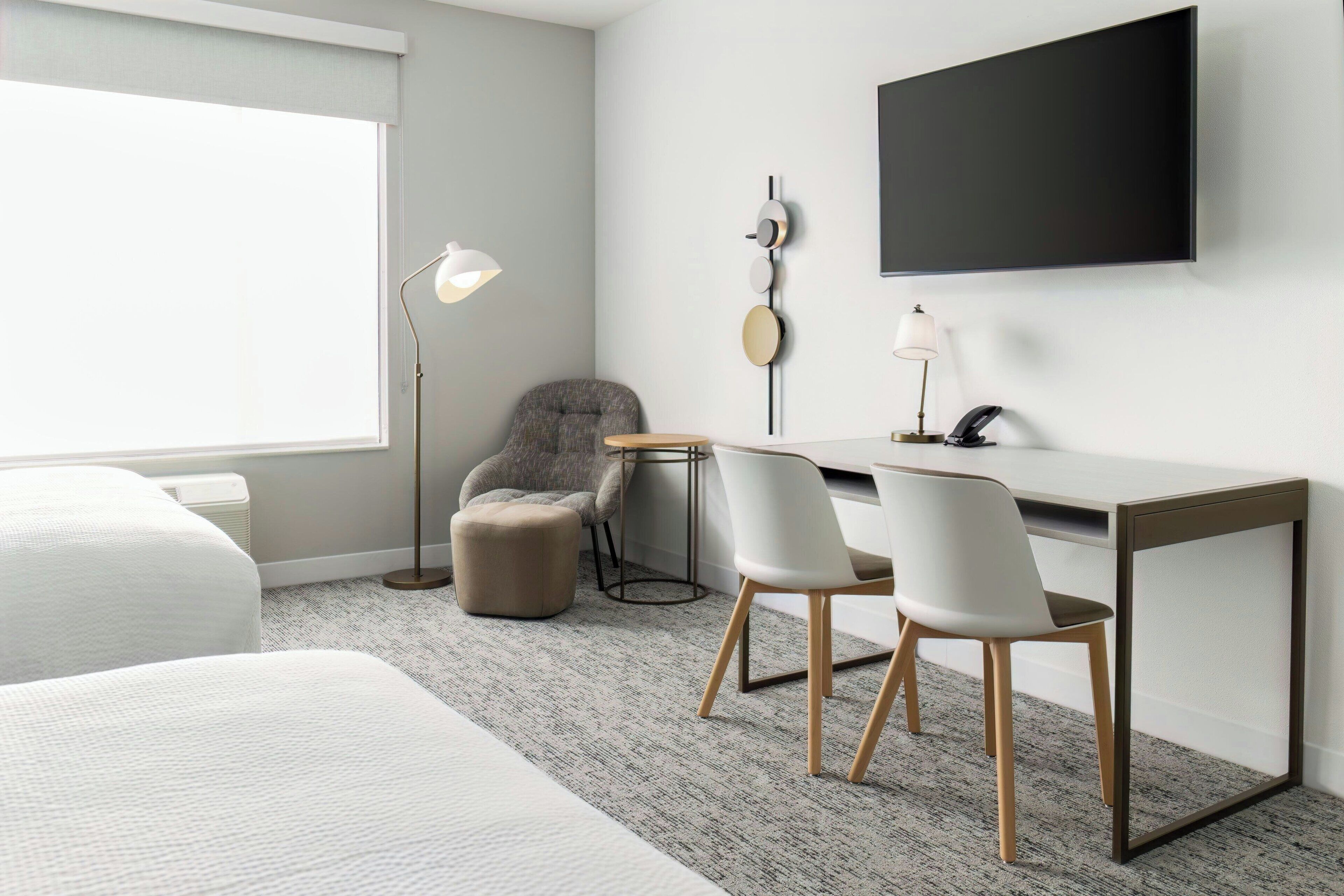 Una habitación de hotel moderna con una cama, un escritorio, dos sillas, un televisor y una lámpara.