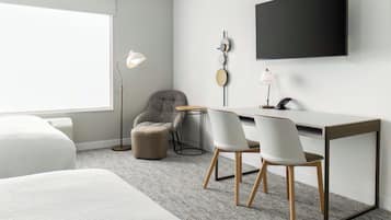 Una habitación de hotel moderna con una cama, un escritorio, dos sillas, un televisor y una lámpara.