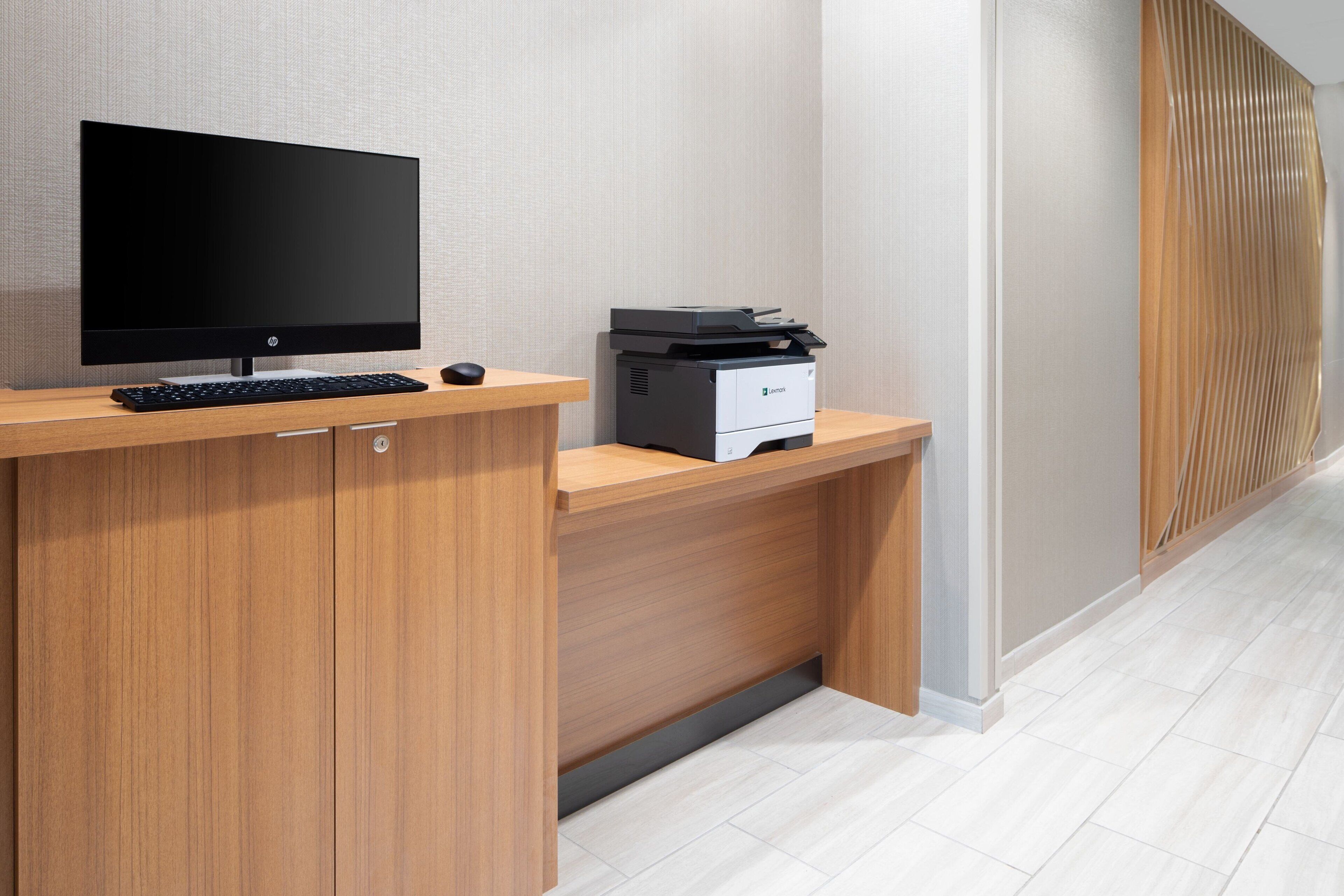 A modern office desk with a flat-screen monitor, keyboard, mouse, and a printer.