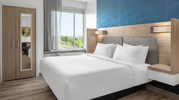 A modern hotel room with a large bed, a wooden wardrobe, a large window with a view, and a geometric wall design.