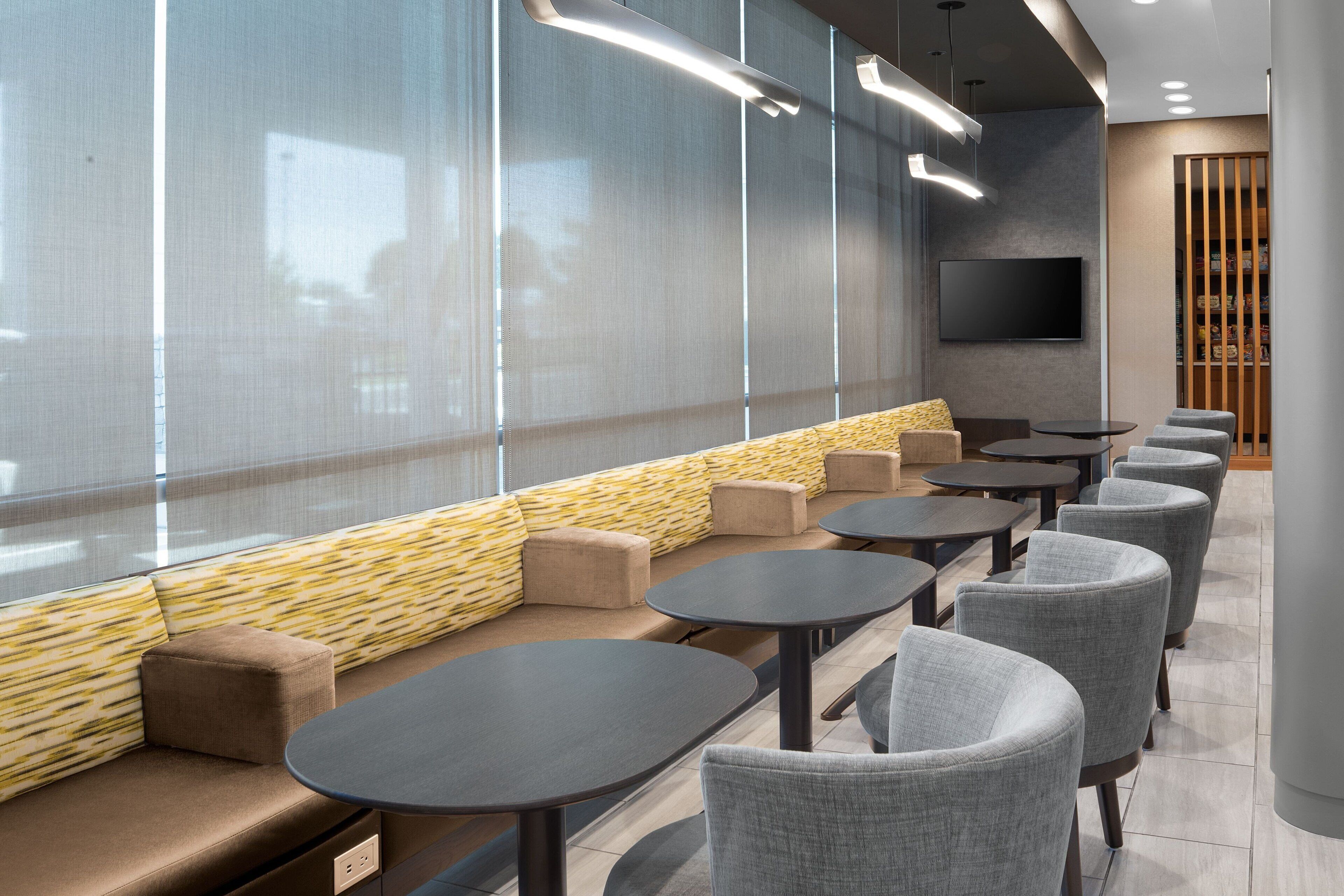 A modern seating area with a sofa and tables, a flat-screen TV, and a view through large windows.