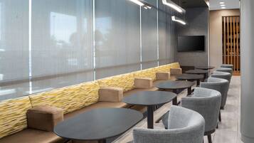 A modern seating area with a sofa and tables, a flat-screen TV, and a view through large windows.