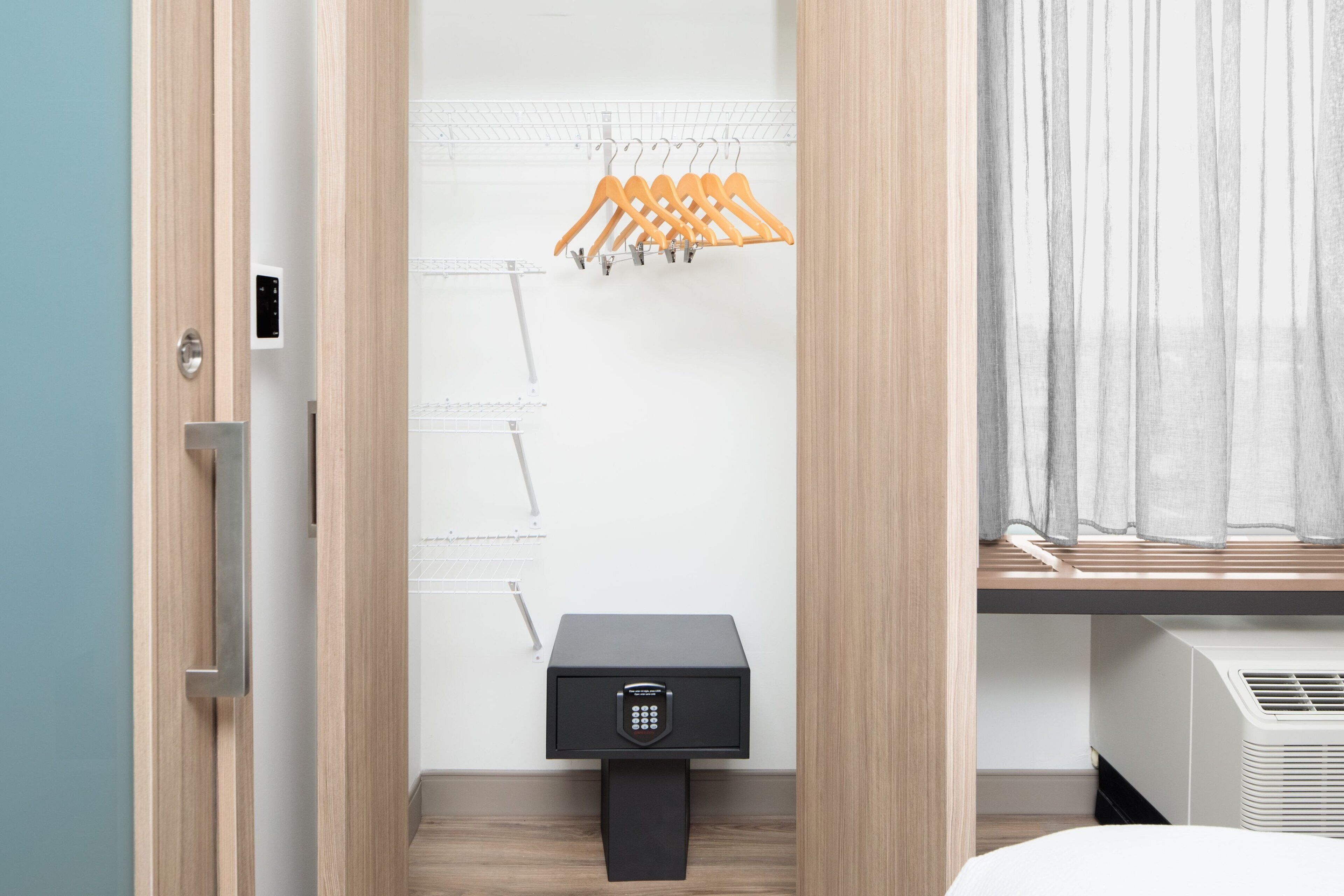 A modern bathroom with a wooden vanity, a black safe, and a drying rack with orange hangers.