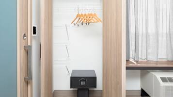 A modern bathroom with a wooden vanity, a black safe, and a drying rack with orange hangers.