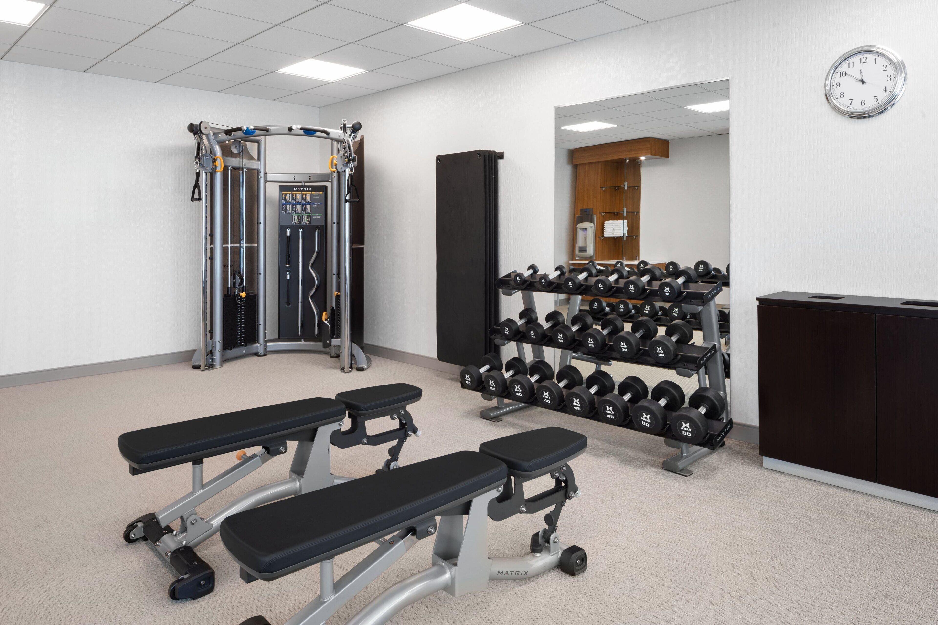 A gym with weightlifting equipment, benches, and a rack of dumbbells.