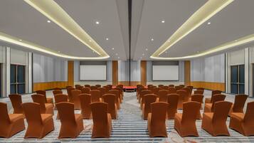 A conference room with rows of orange chairs, a red table, and a large screen at the front.