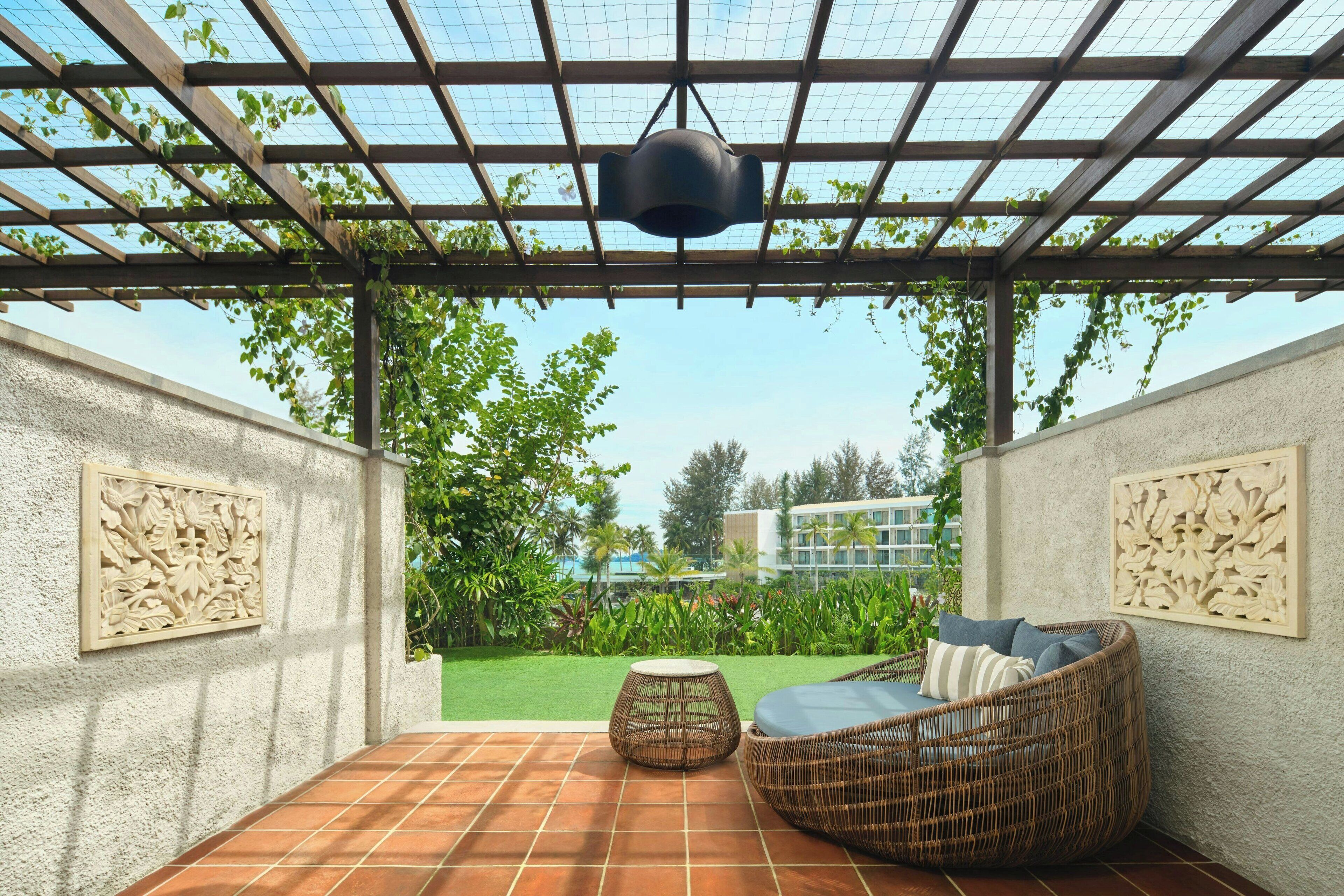 Une terrasse couverte avec un canapé en osier et une table ronde, le tout agrémenté d’une vue sur le jardin.