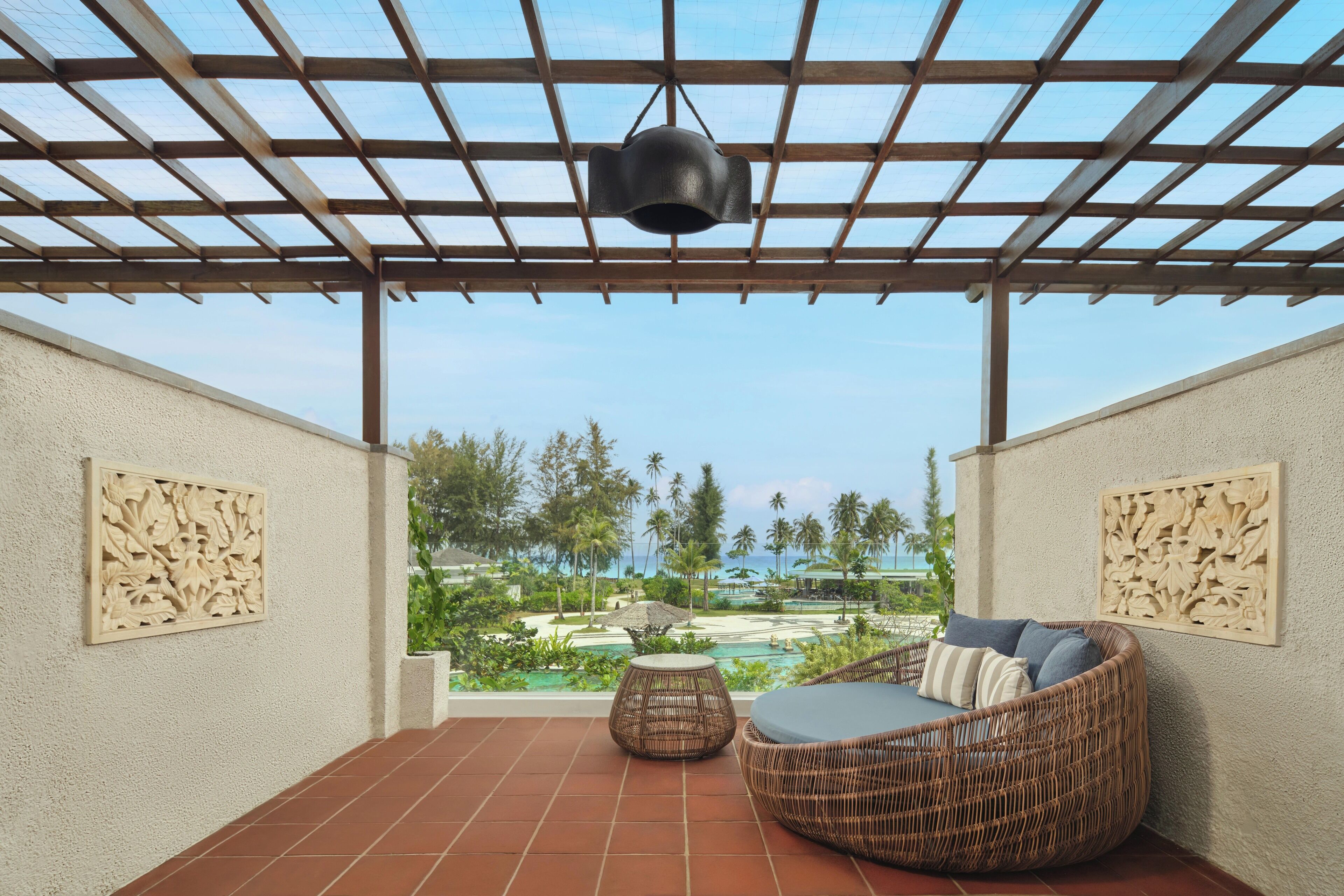 Überdachte Terrasse mit Rattan-Sofa und kleinem runden Tisch, mit Blick auf einen Pool und tropische Landschaft.