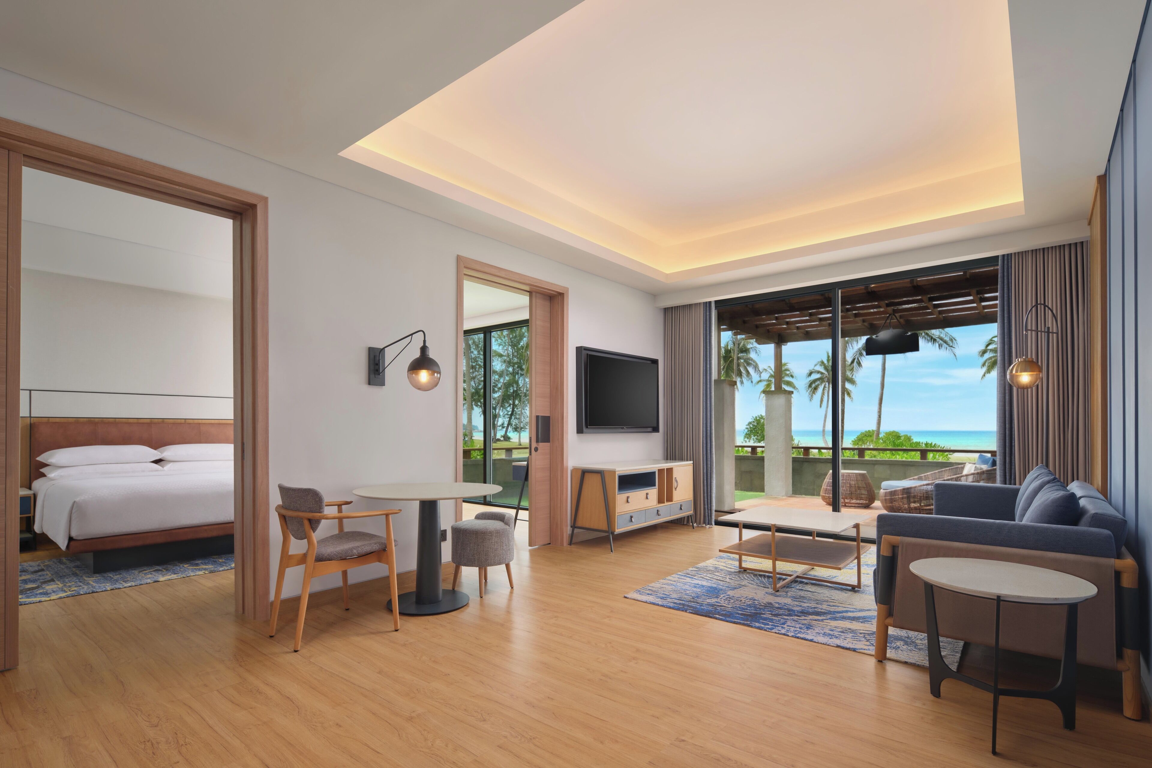 Een moderne hotelkamer met een bed, zithoek, televisie en een balkon met uitzicht op de oceaan.