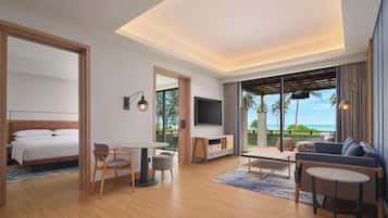 A modern hotel room with a bed, seating area, TV, and a balcony with a view of the ocean.