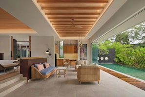 A modern interior with a wooden ceiling, a kitchen area, a seating area with sofas and a dining table, and a view of a swimming pool and greenery. - Four Points By Sheraton Bintan, Lagoi Bay (Bintan)