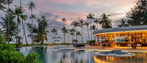 Zona de piscina en un resort, con palmeras, un bar y asientos tipo lounge.