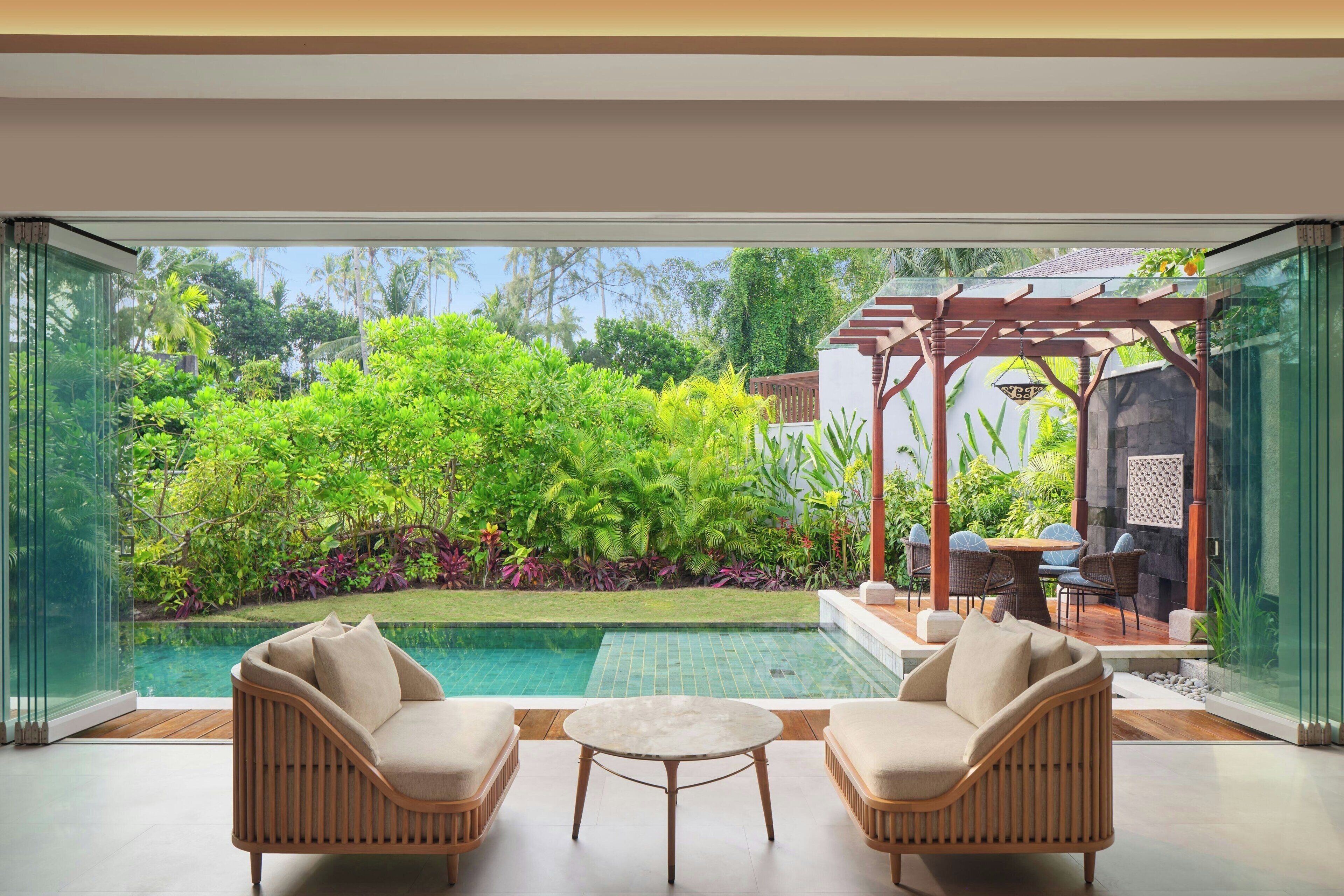 A modern outdoor seating area with a pool, surrounded by lush greenery and a pergola.