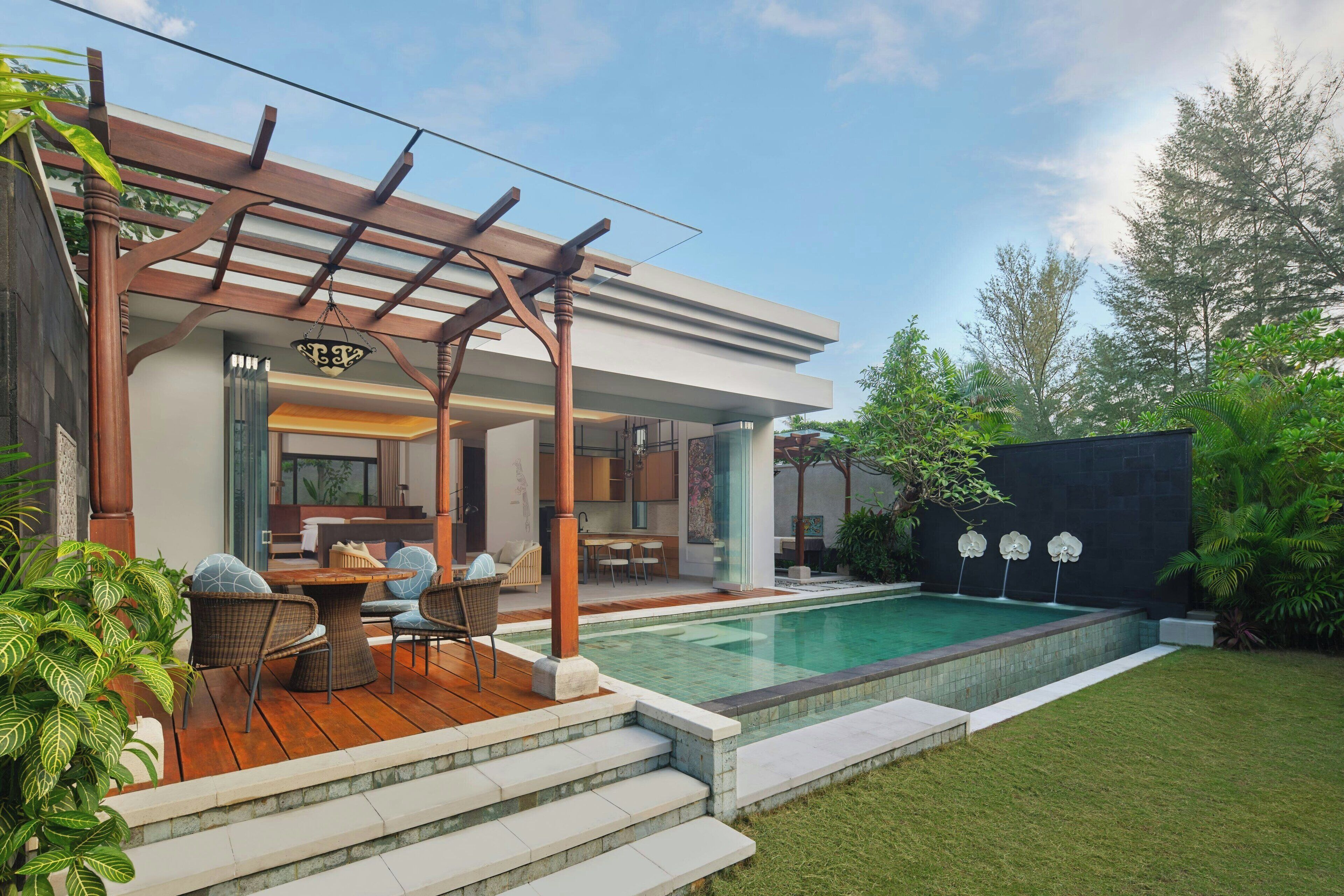 A modern outdoor pool area with a pergola, a dining set, and a well-maintained lawn.