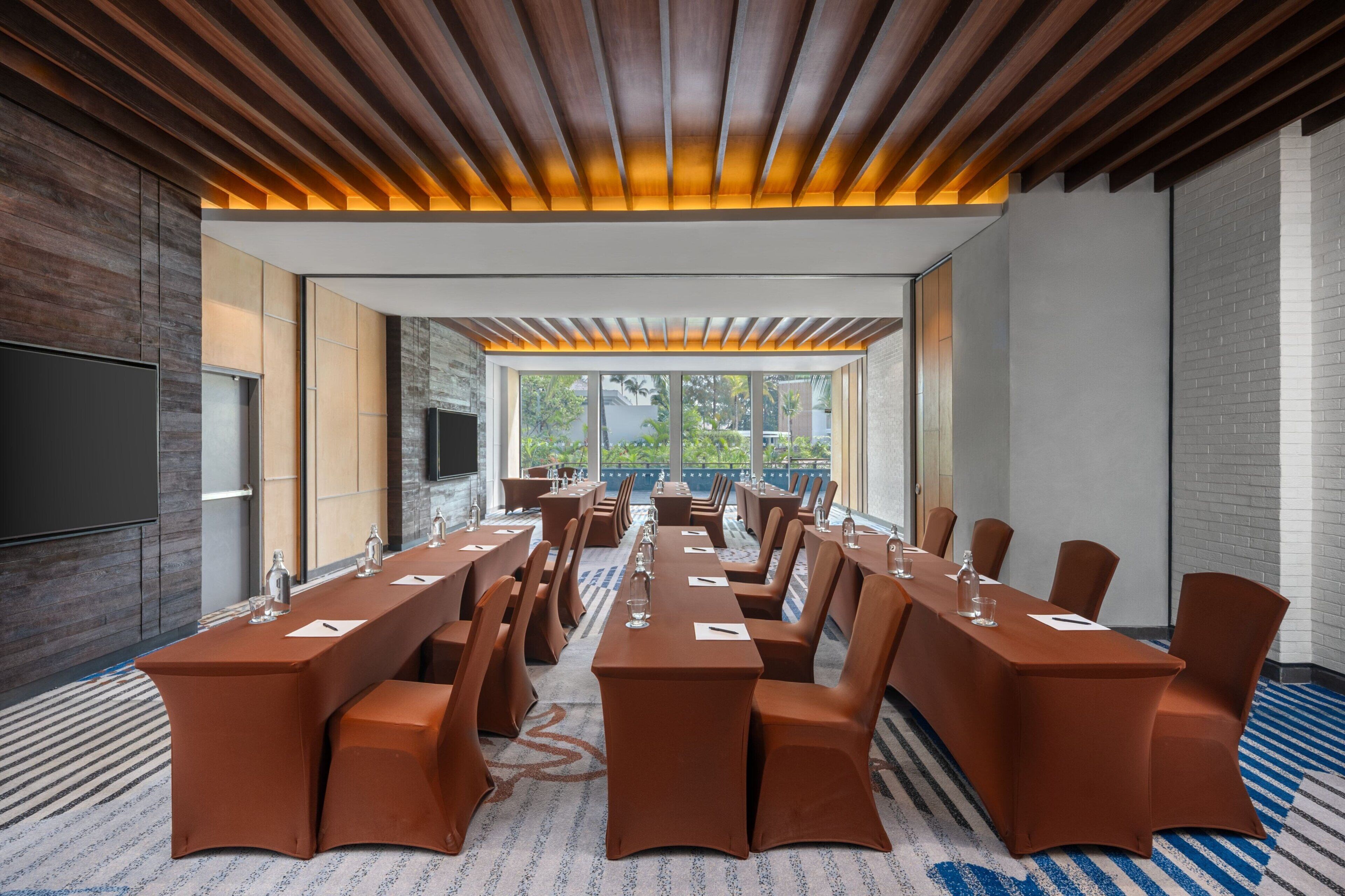 A conference room with a long table, chairs, and a large window providing a view of greenery outside.