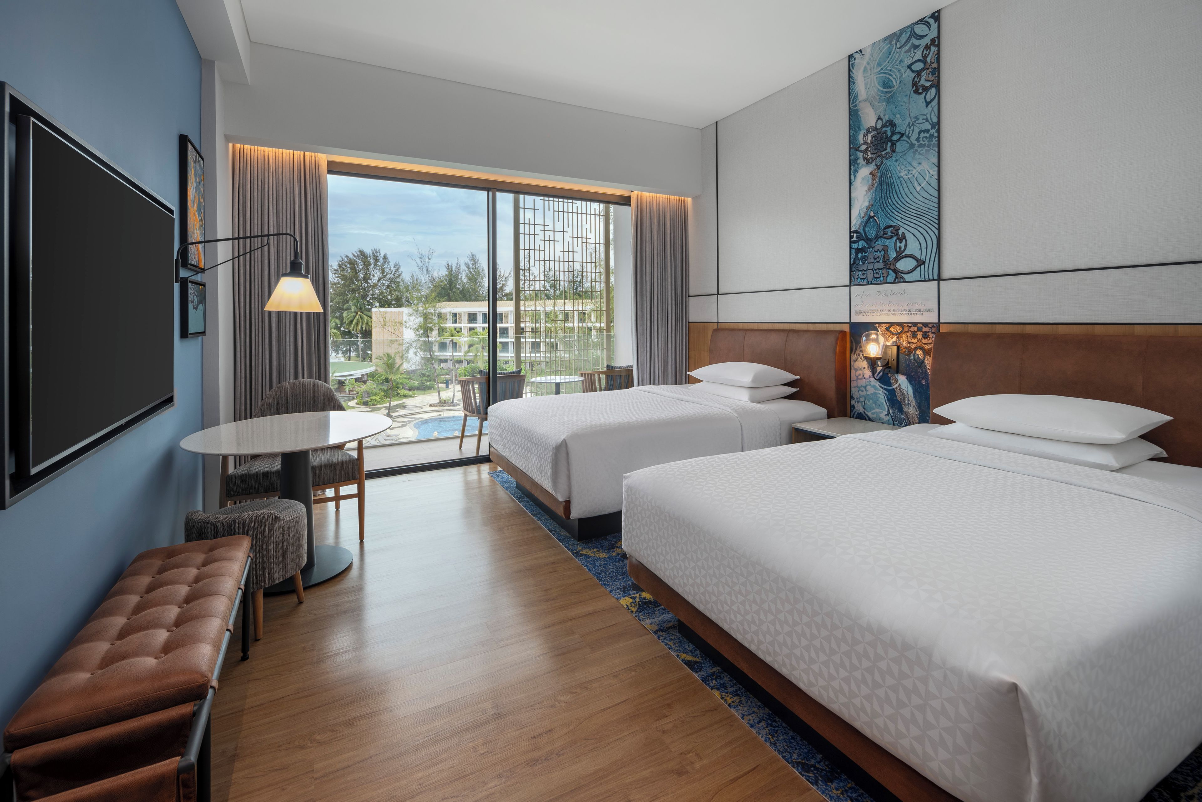 A hotel room with two beds, a desk, and a view of a pool.