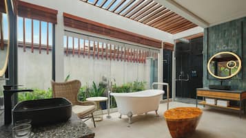 A modern bathroom with a freestanding bathtub, a round mirror, and a wooden coffee table.