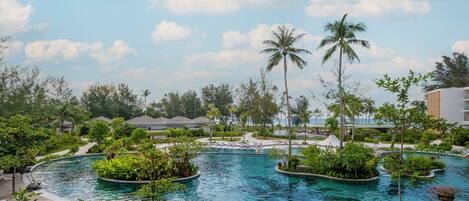 A resort pool surrounded by tropical vegetation and palm trees, with a clear sky above.