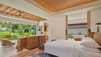 A modern bedroom with a large bed, a sitting area with a sofa and chairs, a small kitchen area, and a view of lush greenery outside.