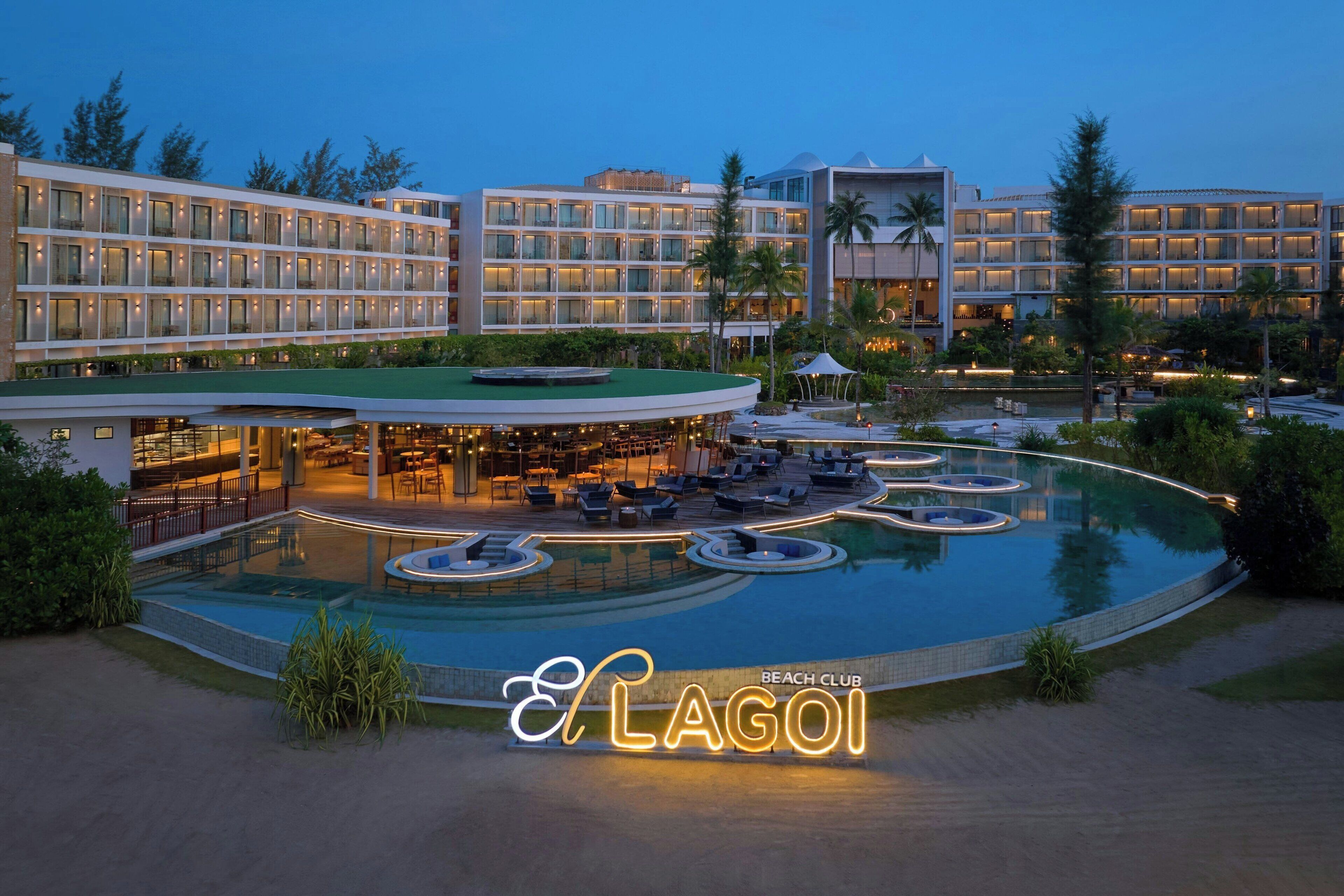 A hotel with a large pool area, multiple hot tubs, and a well-lit outdoor lounge.