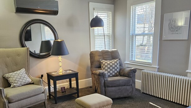 A living room with a beige sofa, a gray armchair, a small ottoman, a black lamp, and a radiator. - Steele Brook Manor
Tranquil get away nestled 
in  Litchfield County.  (Watertown)