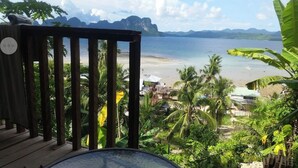 Terraza de madera con vista a una playa, palmeras y una vista del mar y las montañas.
