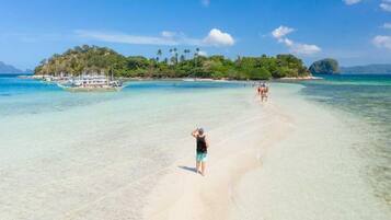 A beach with clear turquoise water, a sandy shore, and a small island with boats in the background.