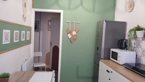 A compact kitchen with a microwave, a refrigerator, and a small dining area with a chair and table. - Hyper Centre-ville Avec Balcon, Idéalement Situé (Saint-Étienne)