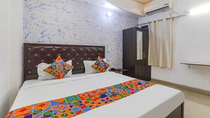 A hotel room with a bed, a headboard, a nightstand, a wardrobe, and a curtain. - Fabexpress Victory (Lucknow)