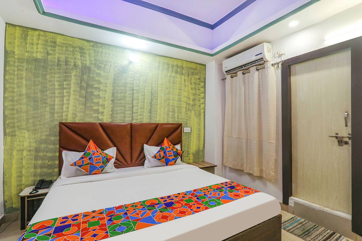 A hotel room with a bed, a nightstand, a wall-mounted air conditioner, and a door.