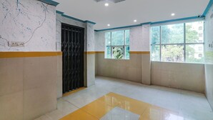 A spacious room with a tiled floor, a black door, and a window with a view of trees. - Fabexpress Victory (Lucknow)