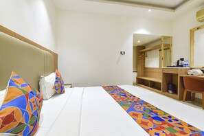 A hotel room with a bed, a desk, a chair, and a mirror.
