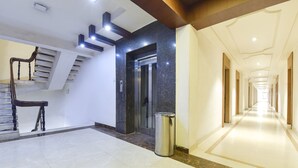 Eine moderne Hotelhalle mit einer Marmortreppe, einem Aufzug und einem langen Korridor.