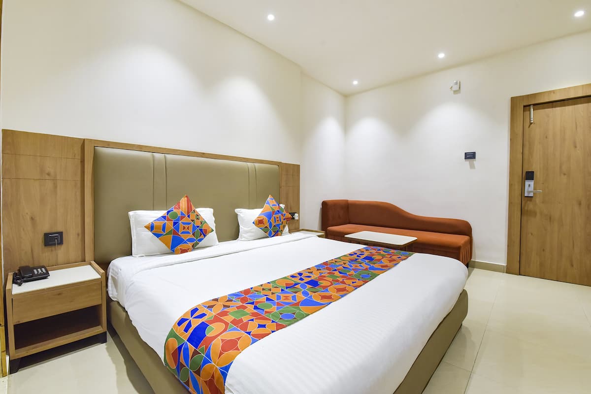 A hotel room with a large bed, a wooden headboard, a nightstand with a phone, and a small table.