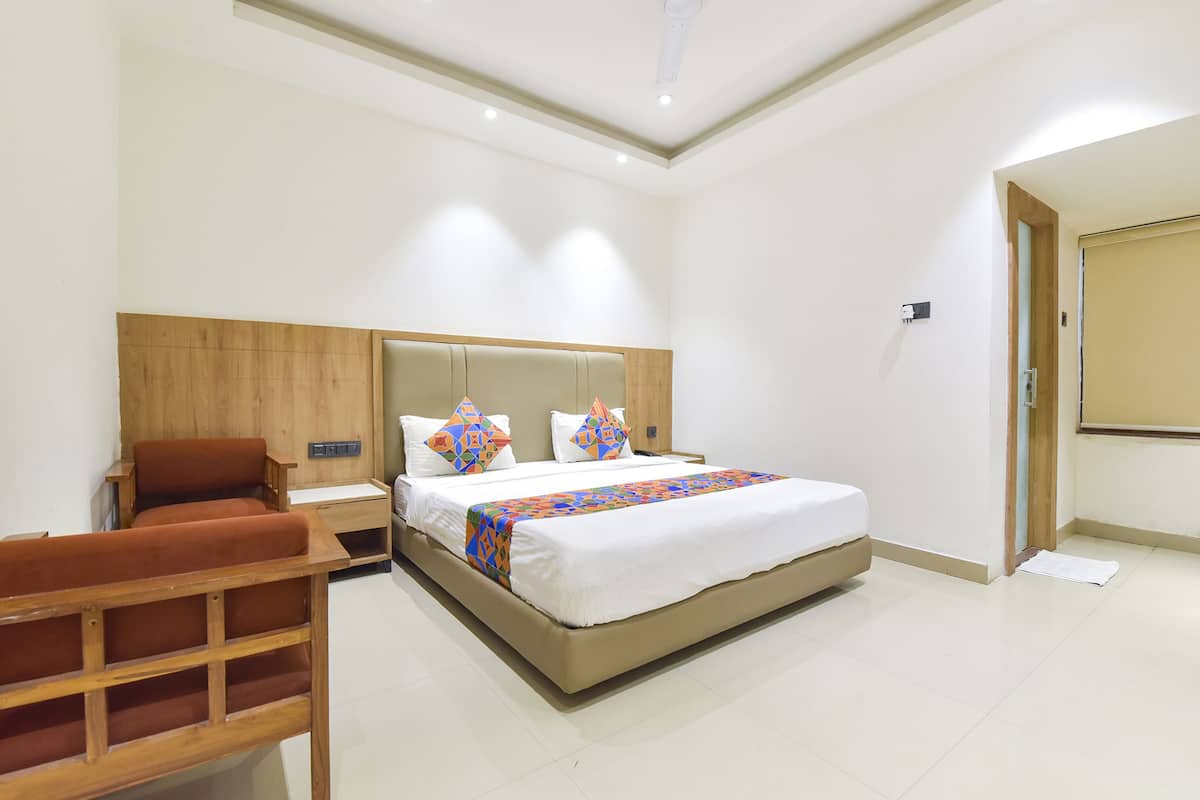 A hotel room with a large bed, a wooden headboard, a nightstand, and a seating area with a chair.
