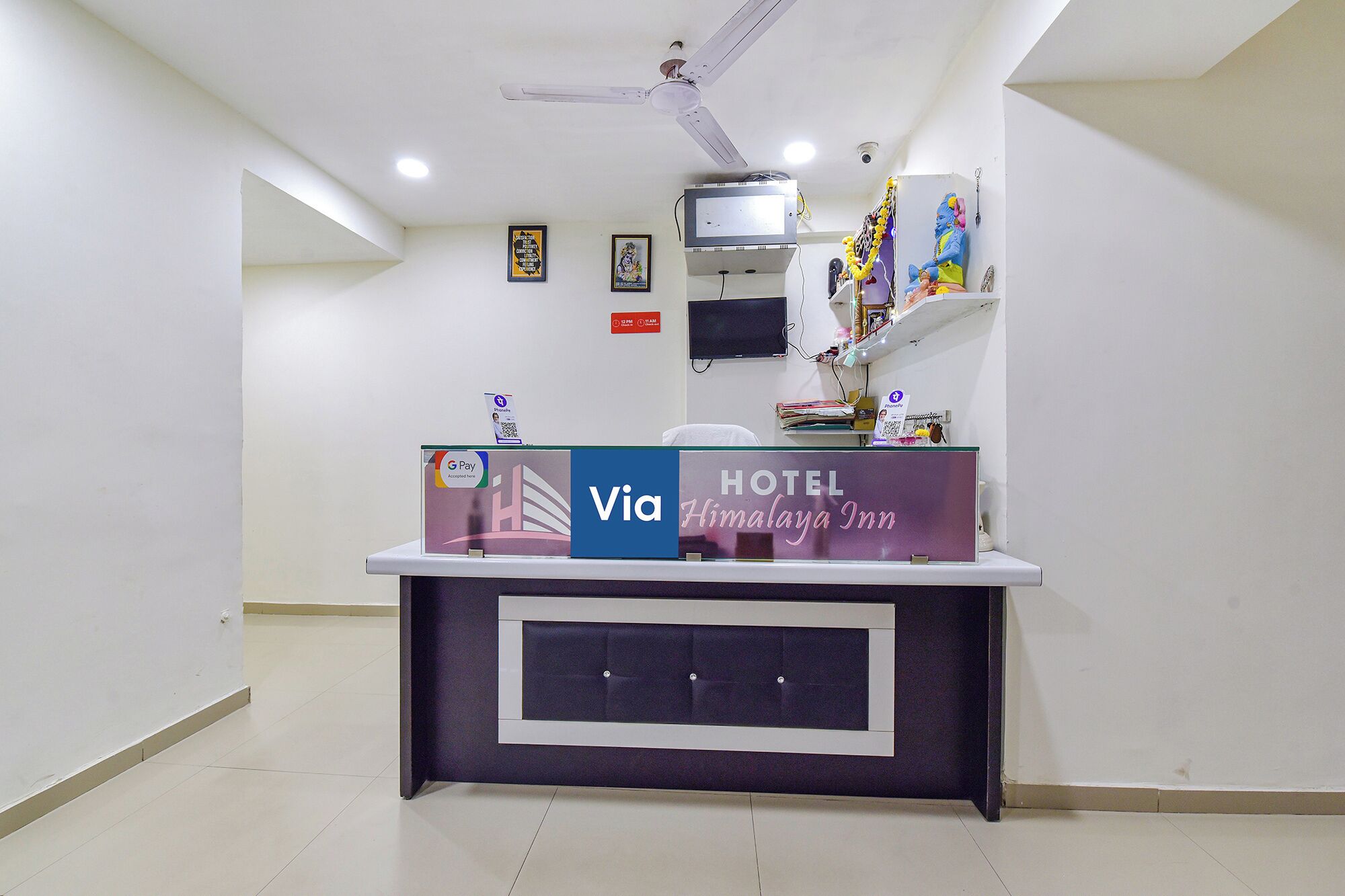 A reception desk with a G Pay and Via sign, a TV, and a framed picture on the wall.