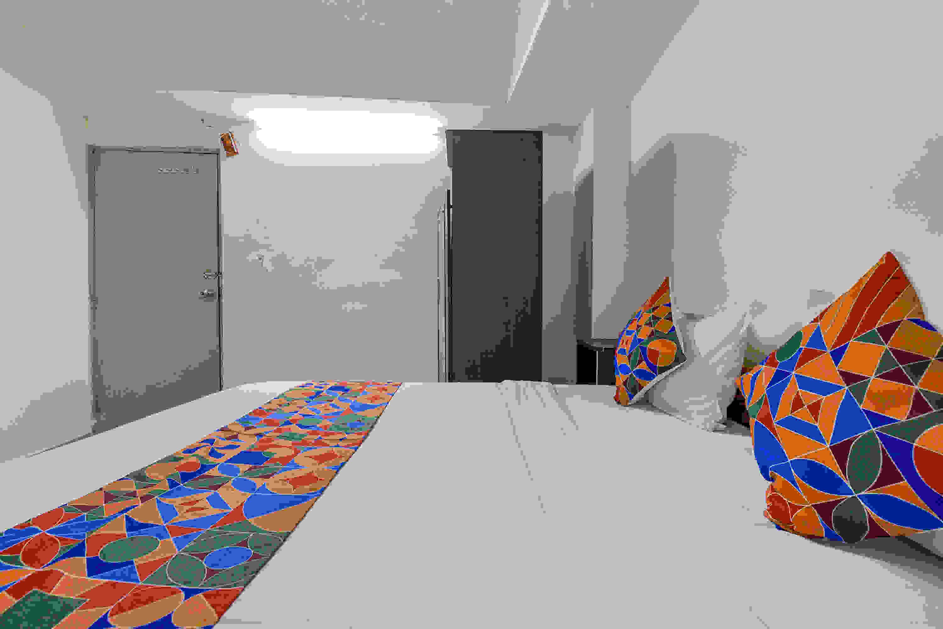 A room with a long, colorful patterned carpet, a bed, and a large, colorful geometric decoration on the wall.