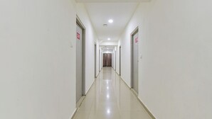 A long, narrow hallway with doors on both sides, a tiled floor, and a ceiling with recessed lighting. - FabExpress Himalaya Inn - Inside Himalaya Mall (Ahmedabad)
