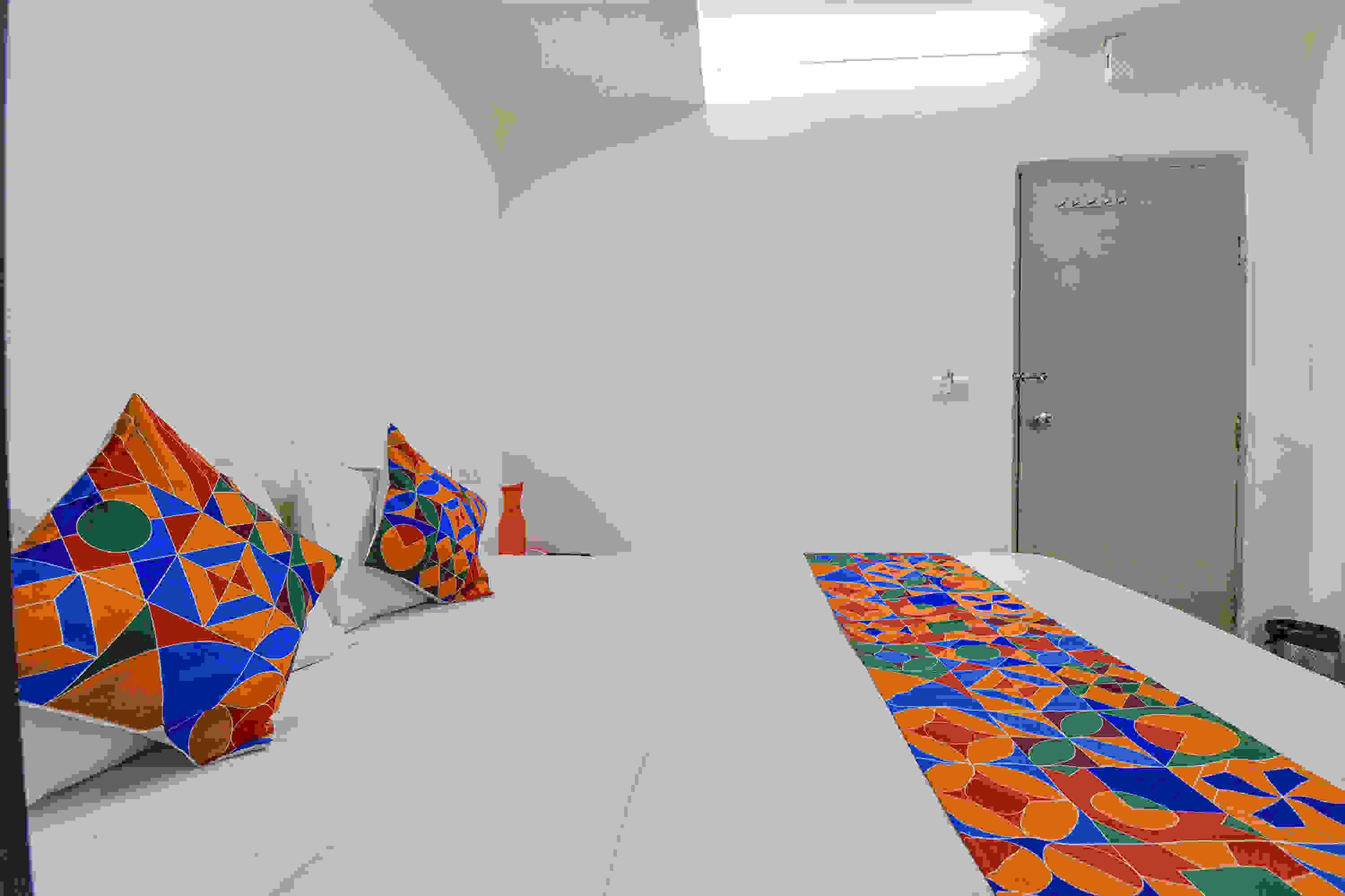 A room with a patterned carpet, a bed with a geometric-patterned bedspread, and a door.