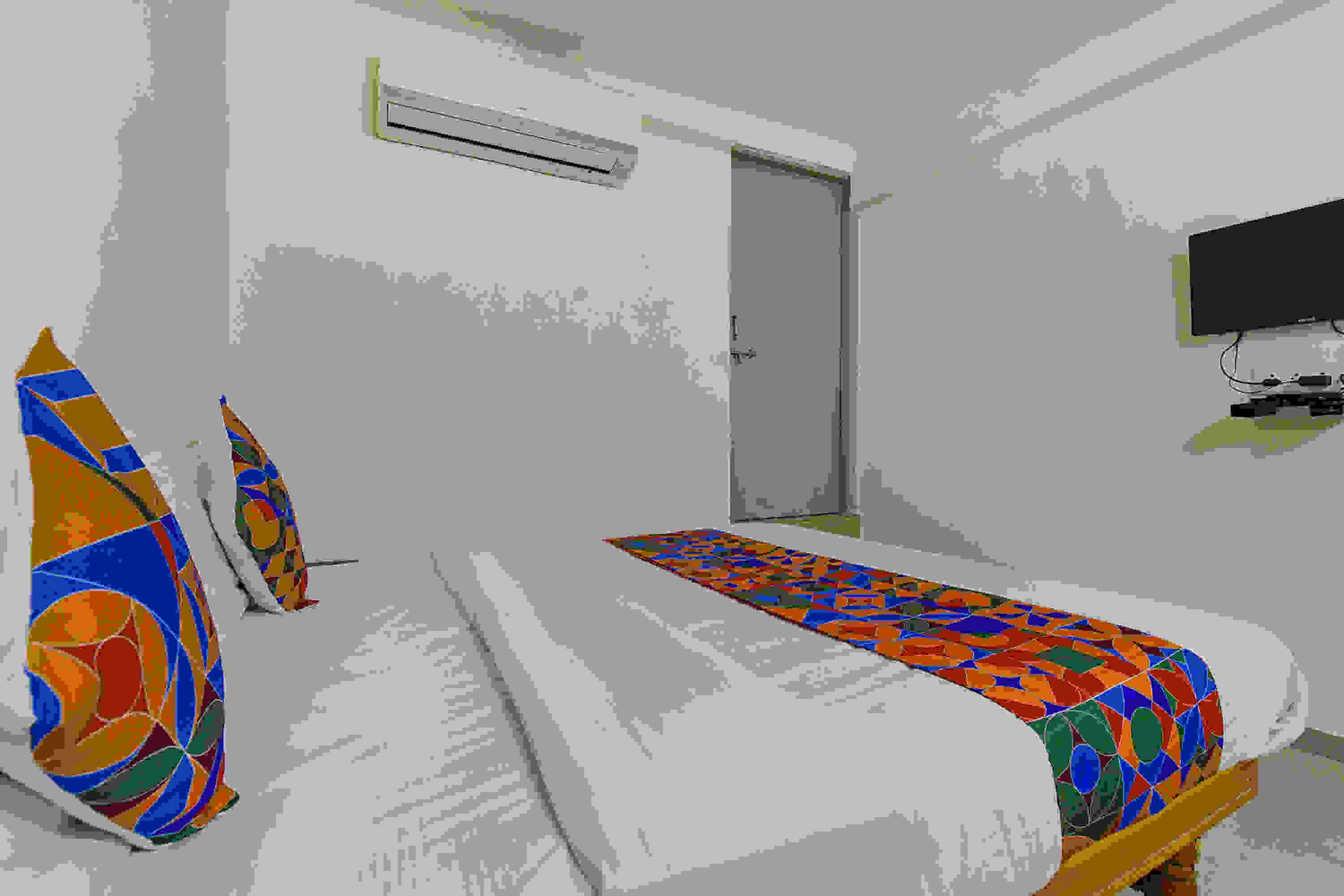 A room with a bed, an air conditioning unit, a television, and a door.