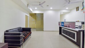 A hotel reception area with a reception desk, a black leather sofa, and ceiling fans. - FabExpress Himalaya Inn - Inside Himalaya Mall (Ahmedabad)
