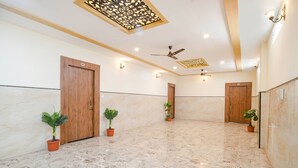 A spacious hallway with marble flooring, wooden doors, ceiling fans, and wall-mounted lights. - Fabhotel Shree Khatu Shyam Palace (Indore)