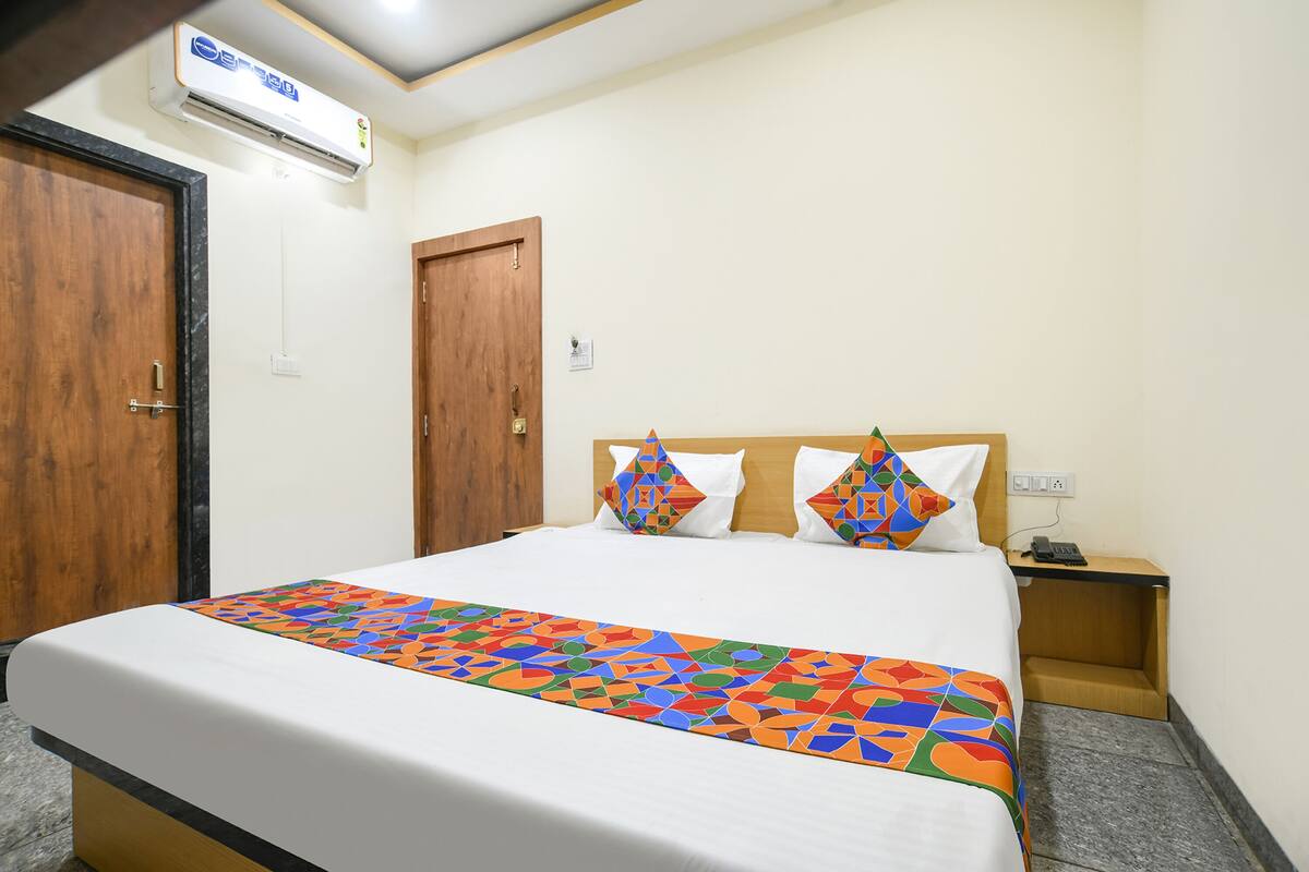 Hotelkamer met een bed, een houten deur, een airconditioning en een nachtkastje met een telefoon.