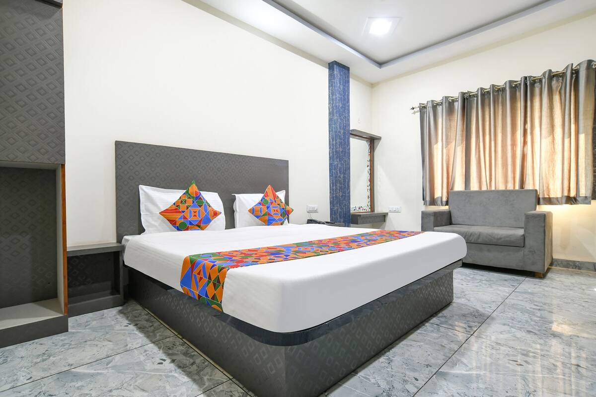 Een hotelkamer met een groot bed, een grijze fauteuil, een nachtkastje en een spiegel.