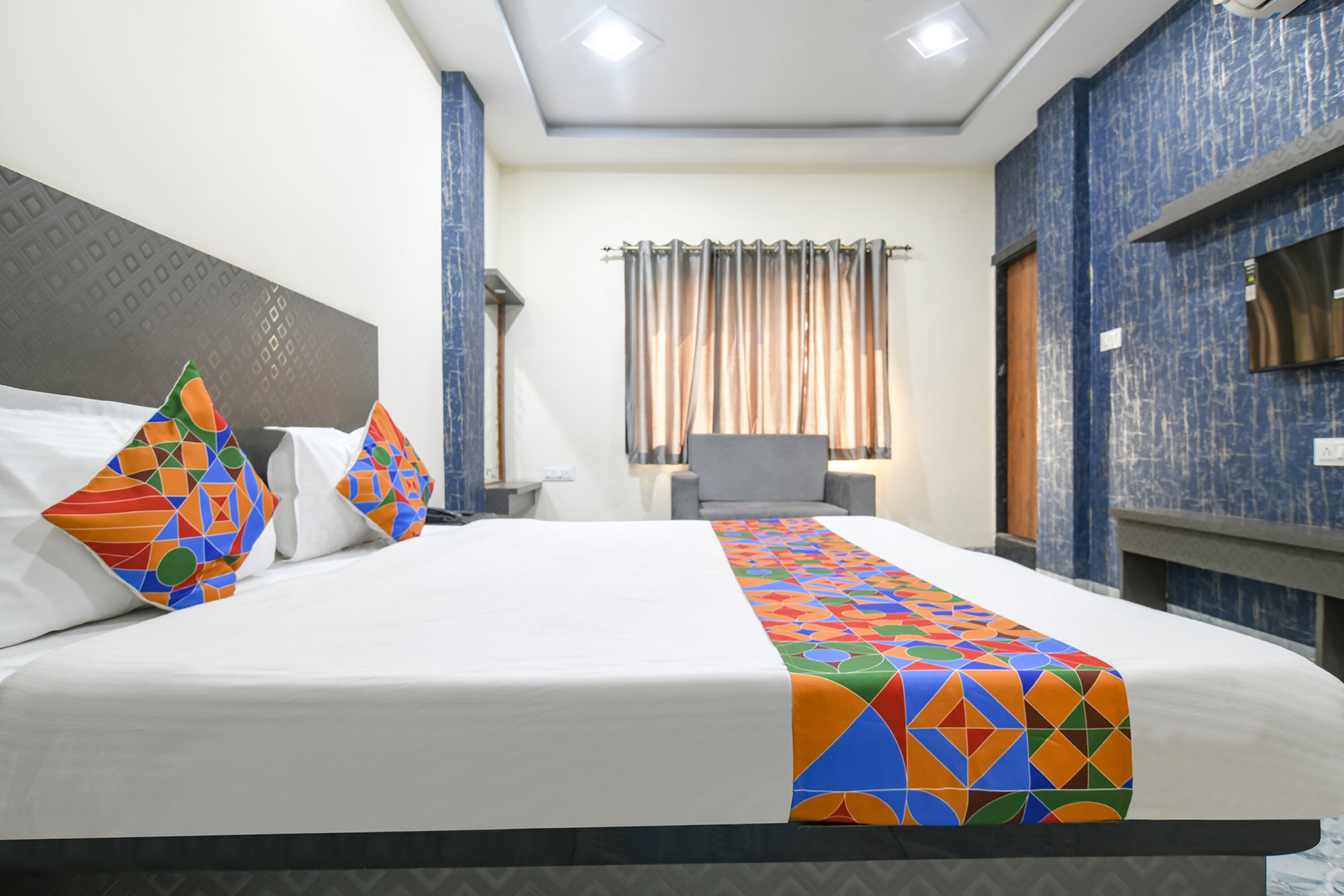 Une chambre d’hôtel avec un grand lit, une télévision, une chaise et une fenêtre avec des rideaux.