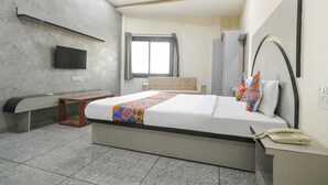 A modern hotel room with a large bed, a bedside table with a telephone, a flat-screen TV mounted on the wall, a window with curtains, and a bench by the window. - Fabhotel Shree Khatu Shyam Palace (Indore)