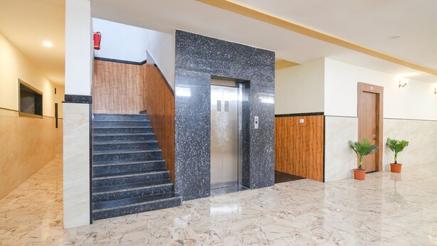 A modern lobby with a marble floor, a wooden staircase, an elevator, and potted plants. - Fabhotel Shree Khatu Shyam Palace (Indore)